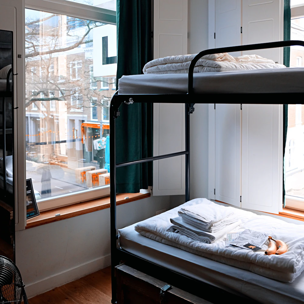 Made-up bunk beds in a bright hostel dorm overlooking the street