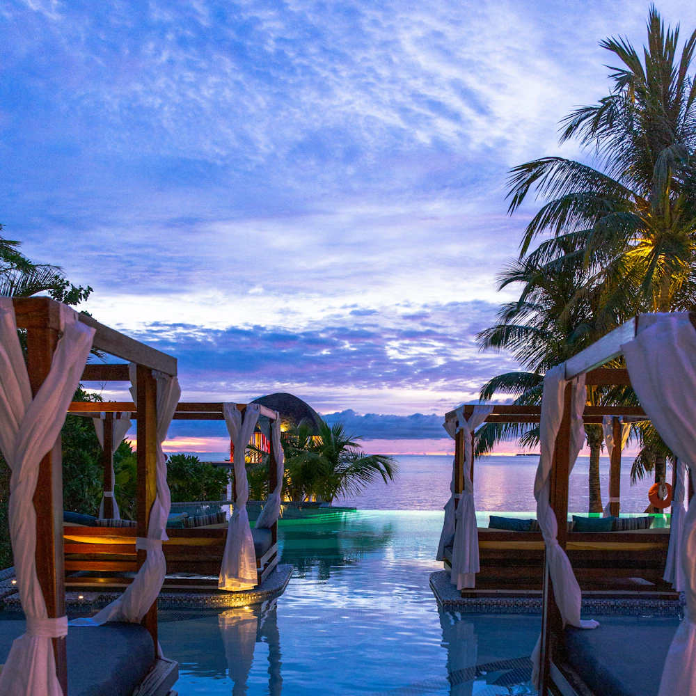 Resort cabanas beside an infinity pool at sunset